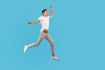 Fototapeta na wymiar Full length, excited man in casual outfit running quickly, hurrying to his dream, walking in air with enthusiastic face, believing in success and luck. indoor studio shot isolated on blue background