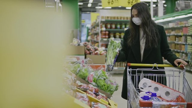 Young woman in medical mask buys food and hygiene items at supermarket during covid-19 coronavirus epidemic. Woman stocks up on food and toilet paper during quarantine and self-isolation