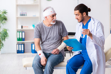Young male doctor and old patient in first aid concept