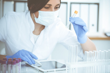 Professional female scientist in protective eyeglasses and mask making experiment with reagents in...