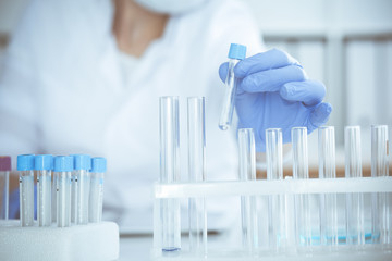 Professional female scientist in protective eyeglasses and mask making experiment with reagents in...