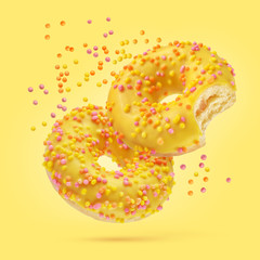 Two glazed donuts on yellow background.