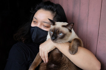 Asian Thai woman carrying a siamese cat and wearing a black cloth mask for prevent the Covid-19 or Corona virus and Epidemic disease at Thailand and around the world. Health and illness concept
