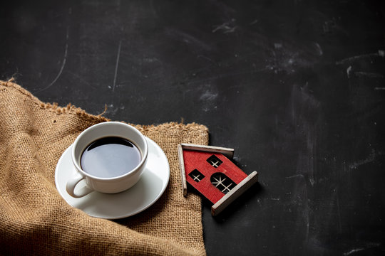 White Cup Of Coffee And Little House On Dark Background