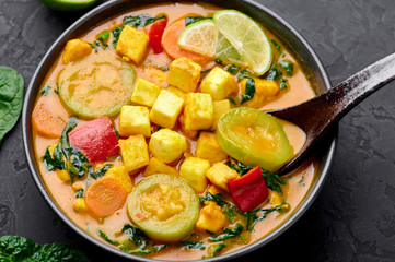 A Yellow Veg Thai Curry with Tofu and vegetables in black bowl at dark slate background. Vegetarian Thai Curry with tofu, zucchini, bell pepper, spinach, carrot. Thai Food. Indian vegetable curry