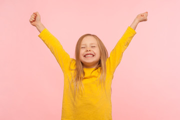 Child sincerely rejoicing success. Cute energetic enthusiastic little girl raising arms in...