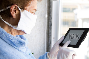 senior woman with medical mask and gloves using tablet at home. quarantine. Corona virus health concept