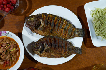 Two grilled fish, beans, salad and strawberry for dinner in restaraunt on an open table.