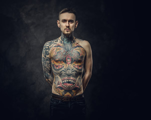 Assertive tattoo artist posing in a dark studio with a half-naked body wearing jeans, tattooed in a...