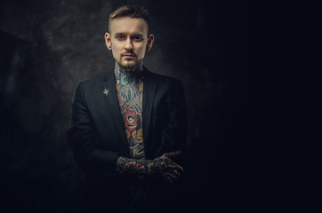 Alternative looking tattoo artist posing on a dark background wearing a black tuxedo on a...