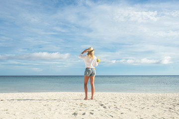 Woman in hat on the beach with coconut.