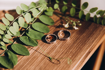wedding rings lie on a wooden table next to the branches of greenery