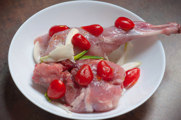 Raw Rabbit Meat, Rear Leg Cuts of Hare Seasoned with Fresh onion, cherry tomatoes and Spices in a white plate