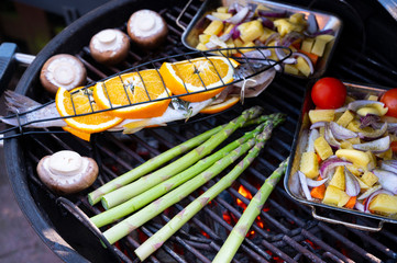 Trout with oranges, mushrooms, asparagus, and pan-fried vegetables with tomatoes, scallions and potatoes on a charcoal grill