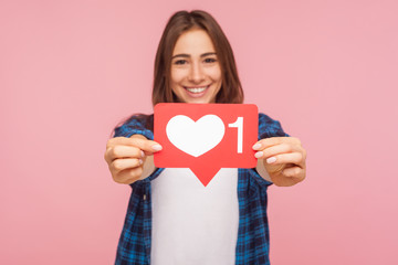 Portrait of happy blogger girl in checkered shirt smiling and showing like icon, heart button to enjoy trendy interesting content in social network. indoor studio shot isolated on pink background