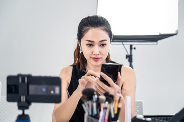 Asian young beauty cosmetic blogger woman use tablet for prepare information before record clip video about demonstrating make up techniques and informing customers about product detail at studio.