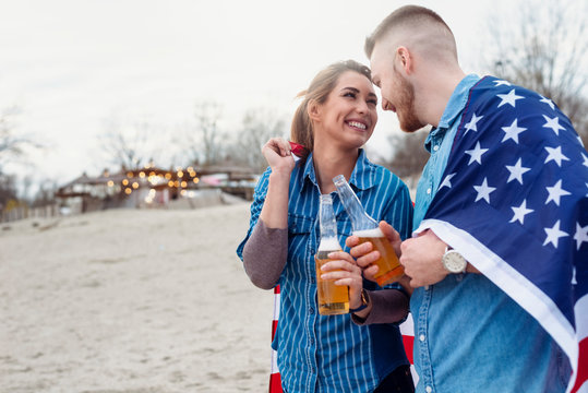 Young beautiful couple with american flag having fun on beach. Teenagers with american flag having fun
