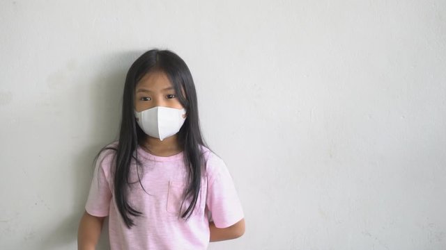 Asian child or kid girl wear N95 paper face mask 3D for close mouth nose and sick with cold cough and protect influenza virus covid 19 or PM2.5 dust smoke with hand up for ban or break stop bacteria