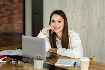 Smiling modern young woman at workplace with laptop