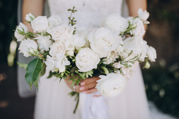 girl in a white wedding dress holds in her hands a bouquet of white flowers with a ribbon