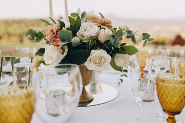 banquet tables are decorated with compositions of flowers and greenery, on the tables are plates with napkins, glasses, candles and name cards