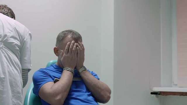 Man sits in chair waiting for doctor to start a procedure. He stuffs his head with hands in despair. Brain examination.