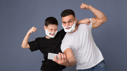 Strong dad and son with shaving foam making selfie on cellphone