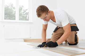 Installation laminate or parquet in the room, worker installing wooden laminate flooring, marking...