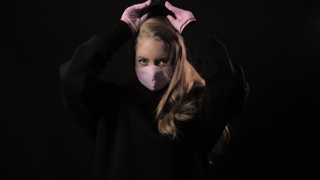 Girl takes off a scary USA mask and underneath is a pink medical mask. Isolated on black background. Health care and medical concept. Close up portrait . 4k. Coronavirus Epidemic, illness, pandemic