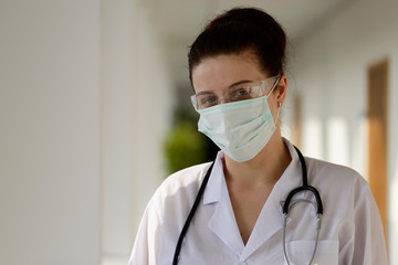 Female doctor scientist in lab coat, defensive eyewear and mask standing indoors. Nurse in white medical uniform.