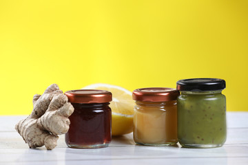 Jar of jam, honey, ginger, lemon on a wooden table, yellow background