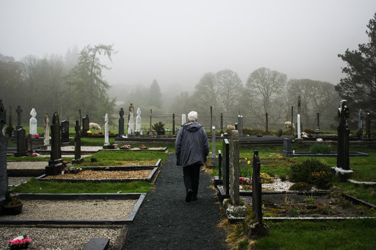 Persona anciana caminando por un cementerio en un d&iacute;a lluvioso de invierno