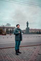 Obraz premium Portrait of a young guy in the background of a monument in the center of the city. Monument to Lenin in Krasnoyarsk. Grey dirty air. Autumn.