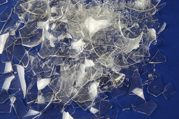 Shattered into 1000 shards concept: View on isolated pile broken glass fragments, blue background