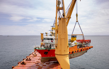 a scientific ship is loaded onto a deck of a heavy lift vessel  by tandem of two cranes with a...