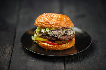 Delicious fresh mushroom burger on a black plate on the dark wooden table, horizontal, side view