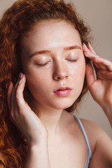 a beautiful red-haired girl washed her face and closed her eyes. Teenage skin care concept. Shot in a studio on a beige background, without makeup, closeup