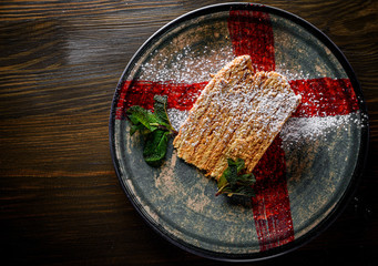 Slice of layered honey cake in a plate on wooden table