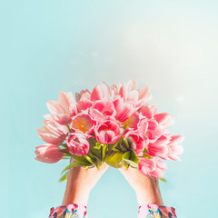 Female hand holding big beautiful pink tulips bunch at blue sky background with sunlight. Close up. Creative greeting. Mothers day concept. Springtime abstract