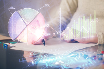 Hand taking notes in notepad. Forex chart holograms in front. Concept of research. Multi exposure