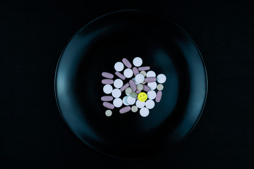 Black plate full of pills one yellow with smile icon
