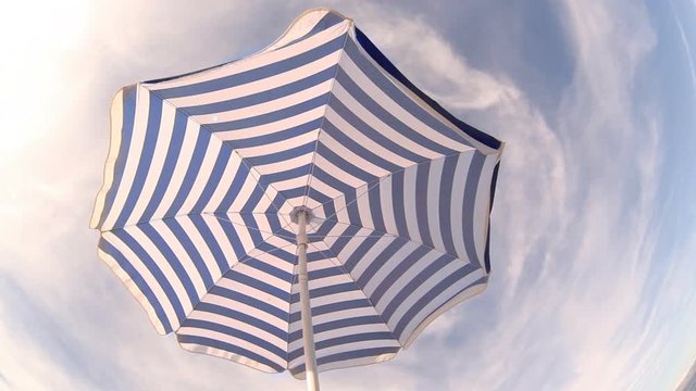 Fish eye footage of striped umbrella fluttering in wind on background of cloudy sky