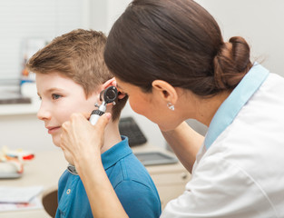 Audiologist examining boy ear , using otoscope, in doctors office. Child receiving a hearing test