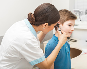Audiologist examining boy ear , using otoscope, in doctors office. Child receiving a hearing exam
