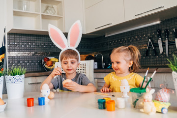 Brother and sister draw eggs. Happy family getting ready for Easter. Cute little baby boy wearing bunny ears. Decorate eggs for Easter.