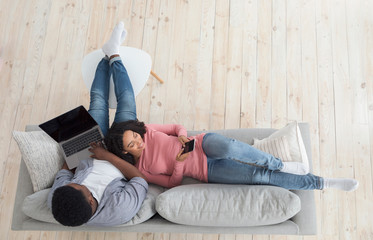 Happy Black Couple Spending Time At Home With Laptop And Smartphone