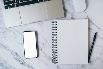Modern marble office desk table with laptop, blank white mobile phone screen mockup and notebook page for input text or entry short note, copy space for creative content and design. Top view, flat lay