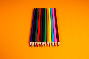 multicolored pencils for drawing stacked on an orange background. Stationery items