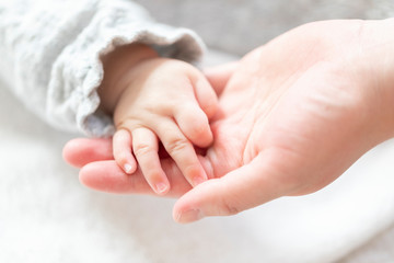 明るい部屋の中で赤ちゃんの手を握る母親の手