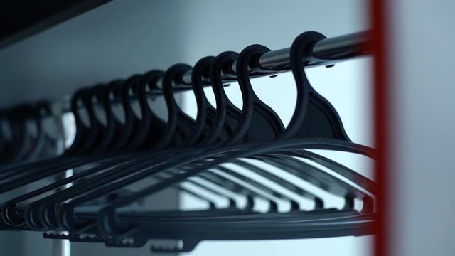 Close-up of swinging empty closet hangers are hanging on the crossbar. Tracking shot in slow motion.